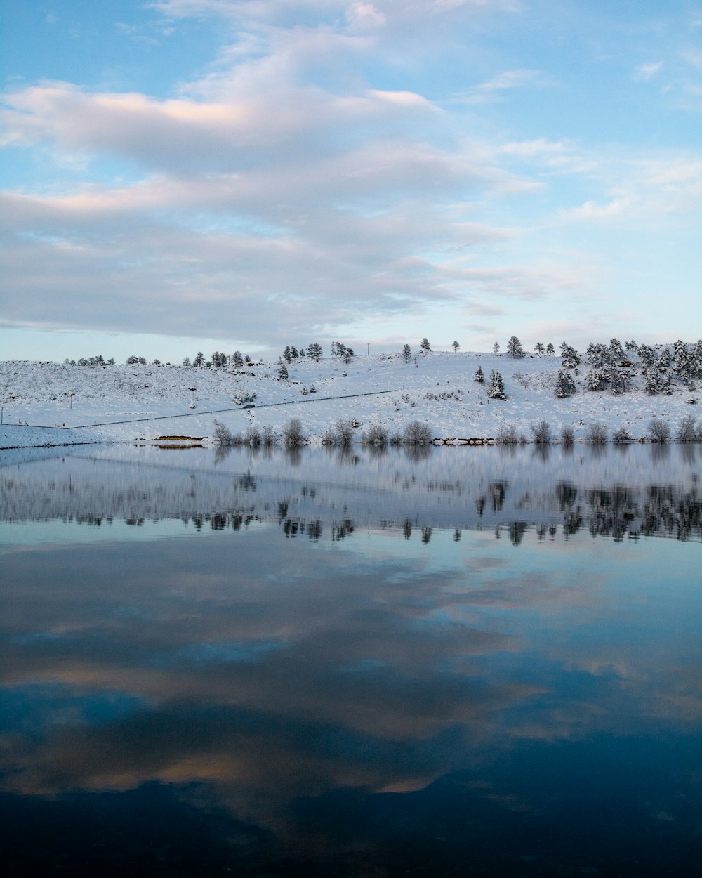 body of water with snow covered ground under cloudy sky during daytime