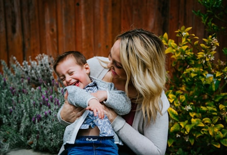 woman in gray sweater carrying baby in blue and white shirt