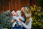 woman in gray sweater carrying baby in blue and white shirt
