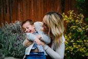A smiling nanny playing with children in a bright, sunlit garden.
