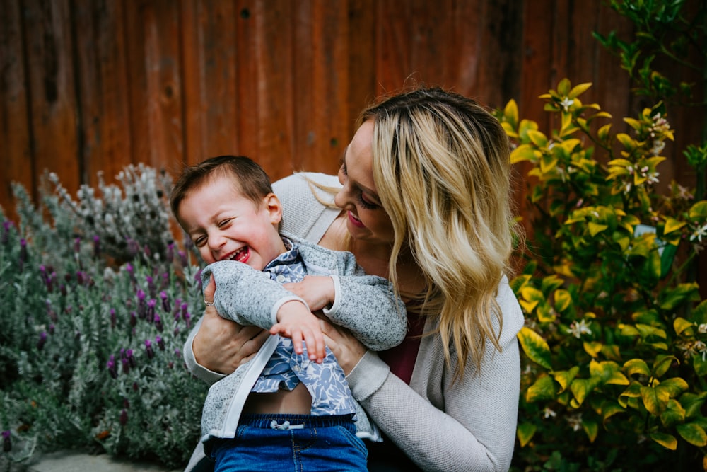 donna in maglione grigio che trasporta il bambino in camicia blu e bianca