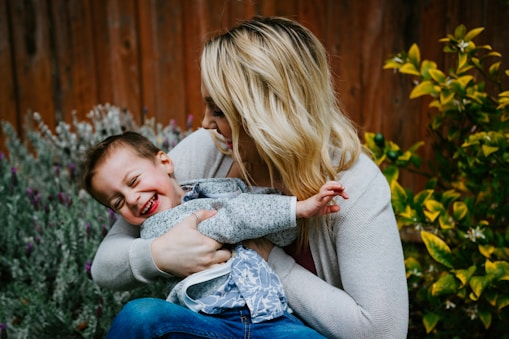 woman in gray sweater carrying girl in blue denim jacket