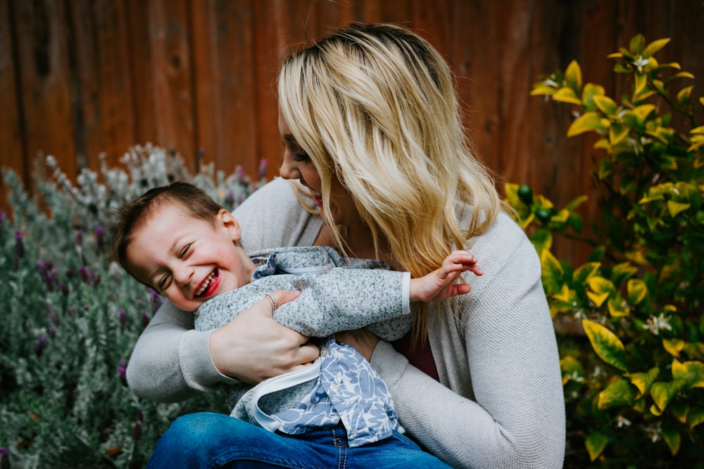 woman in gray sweater carrying girl in blue denim jacket