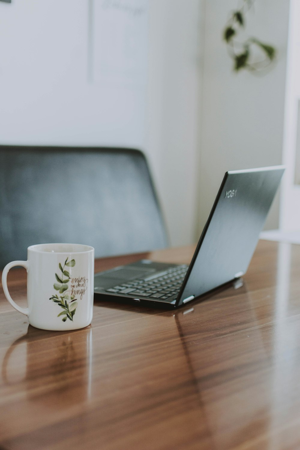 macbook pro beside white ceramic mug on brown wooden table