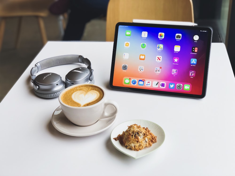 white ceramic cup on white ceramic saucer beside black ipad