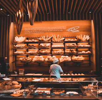 Warm, inviting bakery interior showing shelves filled with a variety of breads and a smiling baker at work.