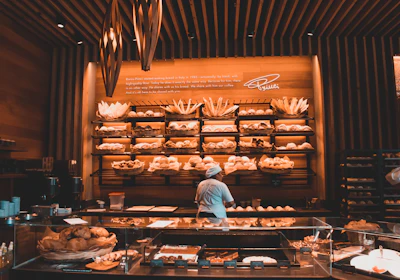 Warm, inviting bakery interior showing shelves filled with a variety of breads and a smiling baker at work.