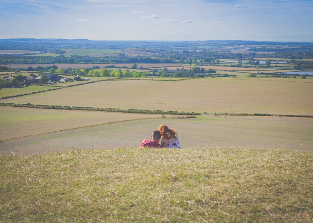 woman in pink jacket sitting on green grass field during daytime