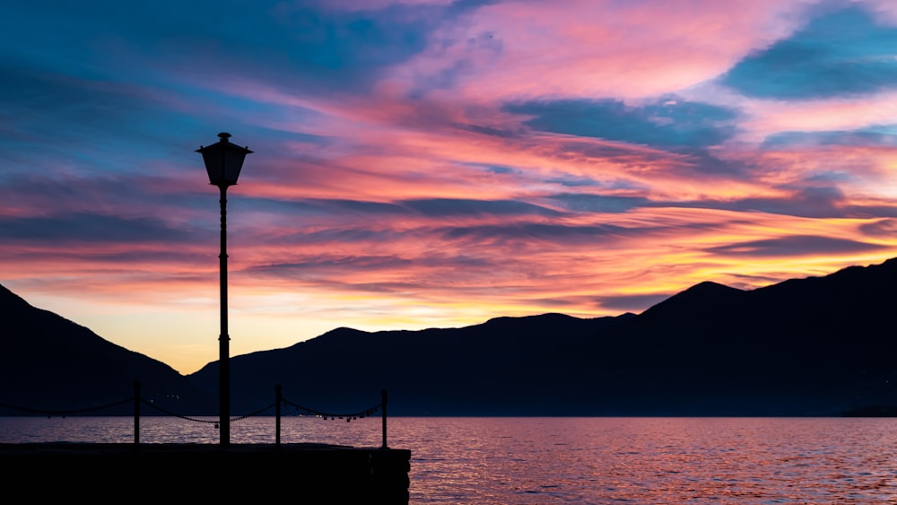 silhouette of person sitting on bench near body of water during sunset