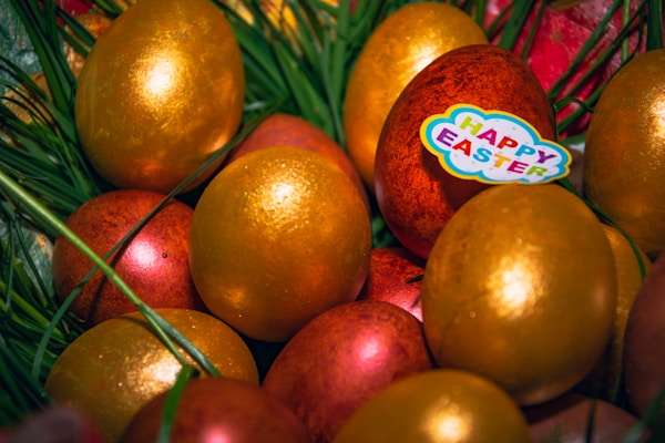 A collection of golden and reddish Easter eggs nestled among green grass with a 'Happy Easter' sticker decorating one of them.
