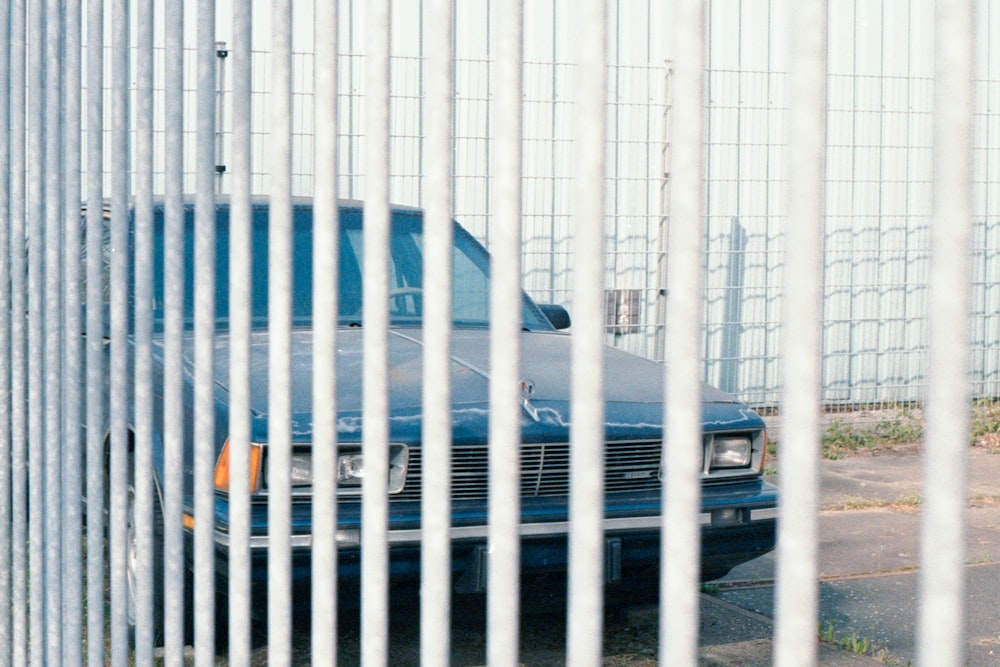 blue car parked beside white metal fence