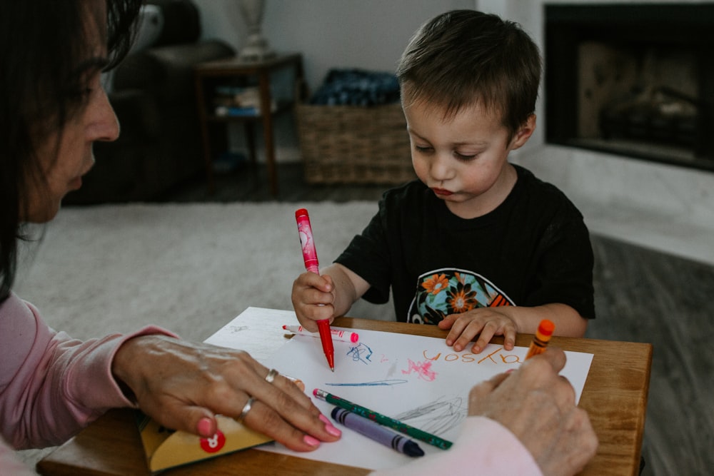 boy in black crew neck t-shirt holding pink pen writing on white paper