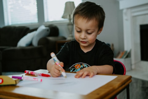 boy in black crew neck long sleeve shirt writing on white paper