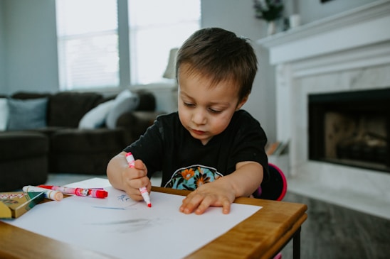 boy in black crew neck shirt writing on white paper