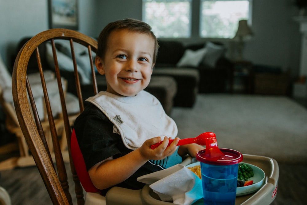 boy in black t-shirt sitting on brown wooden chair