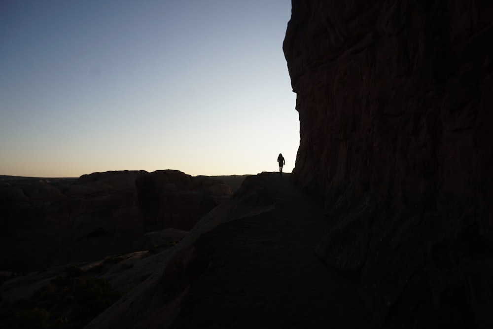 silhouette of person standing on rock formation during daytime