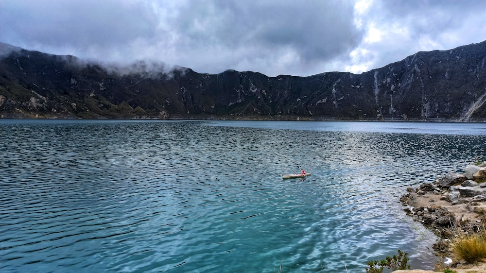 person riding on white and orange boat on sea near mountain during daytime