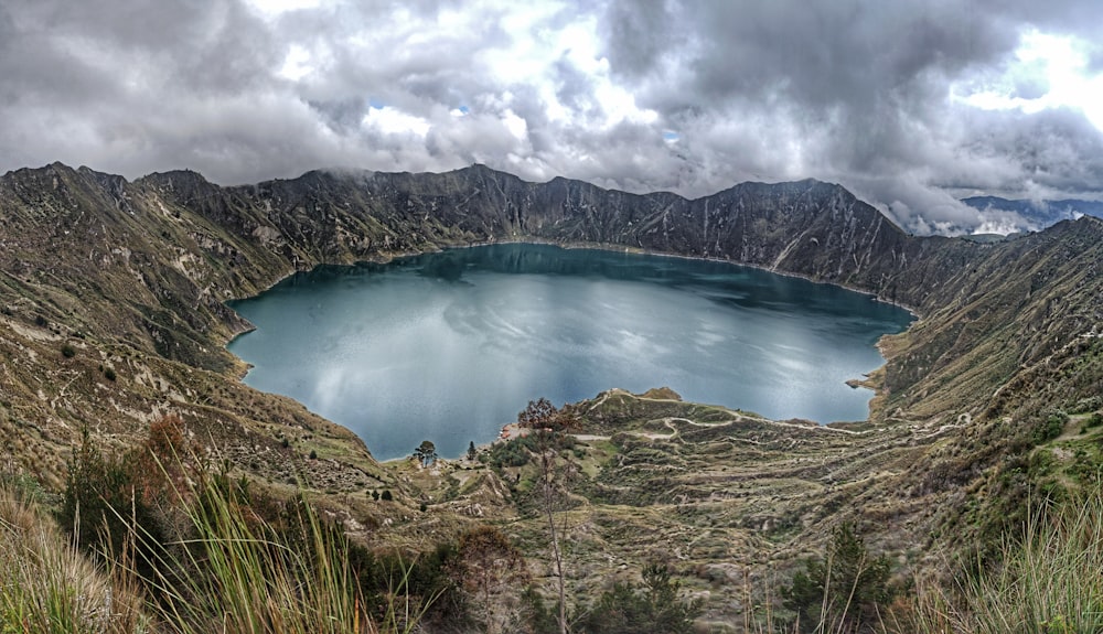 montaña verde y marrón junto al lago azul bajo nubes blancas y cielo azul durante el día