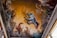 A dramatic painting on a ceiling depicts a person in a flowing garment falling or floating amidst a chaotic scene. Surrounding the figure are mythological or fantastical elements, including horses and winged creatures shrouded in swirling mist and dynamic, architectural structures. The lighting and details convey movement and tension.
