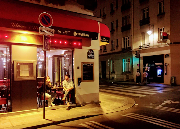 A cozy urban scene at night in Saint-Étienne with warm street lights and a casual couple chatting on their phones.