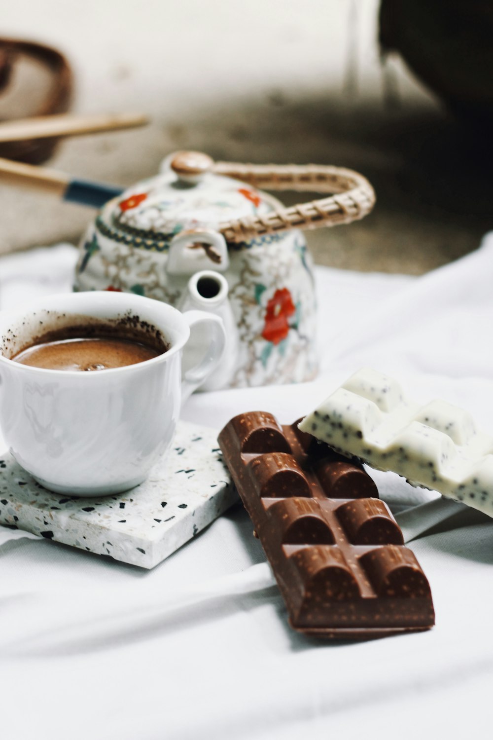 white ceramic cup with coffee beside chocolate bar on white ceramic plate