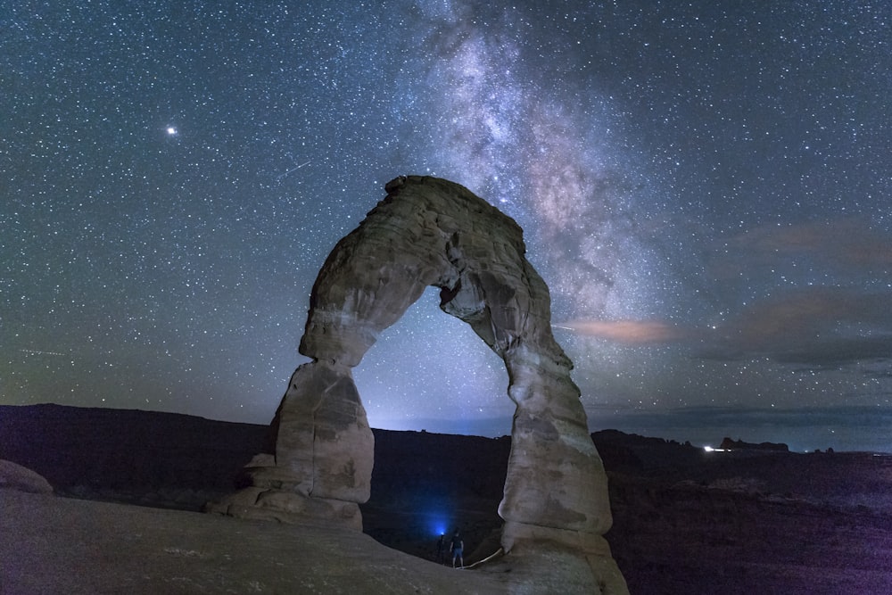 man in black jacket standing on rock formation under starry night