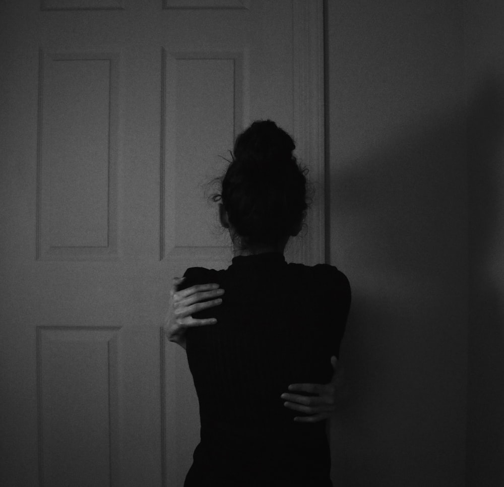 Femme en robe noire debout près d’une porte en bois blanc