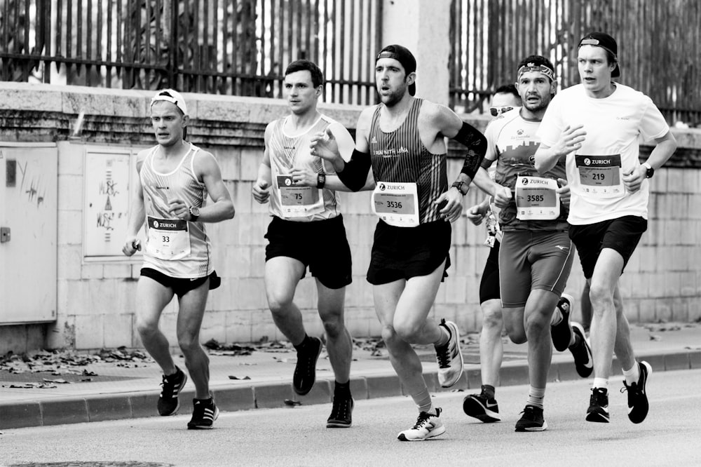 grayscale photo of 3 men running on road