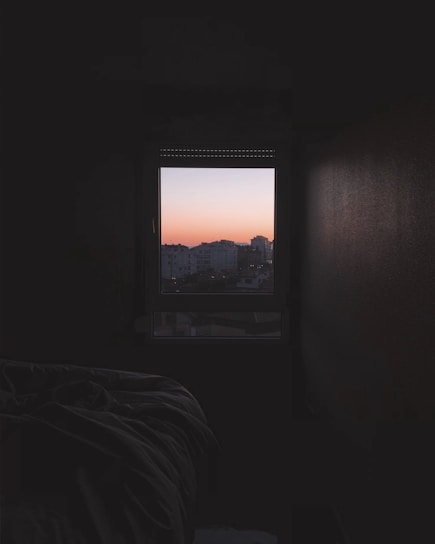 Bright, cozy hotel suite with a large window showing a city skyline at sunset.