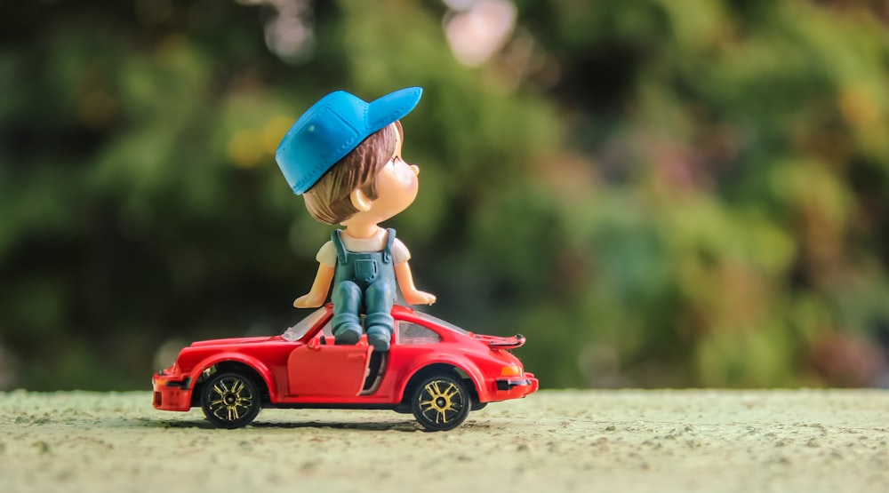 boy in blue and red hat riding red car toy