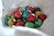 A collection of colorful, speckled eggs nestled in a soft, white, textured cloth. The eggs vary in color, featuring shades of red, yellow, green, blue, and purple, each with black speckles that add to their decorative appearance.