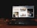 A laptop displaying a website with various images including a woman sitting indoors, a moving race car, a cabin in a mountainous area, and a dog. The device is placed on a wooden table with a glass of water and a notebook nearby, in a dimly lit environment.