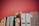 A collection of books arranged vertically next to a ceramic vase with pink flowers on a shelf. White document holders are lined up beside them against a red background.