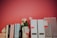A collection of books arranged vertically next to a ceramic vase with pink flowers on a shelf. White document holders are lined up beside them against a red background.