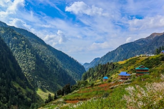 green grass field near green mountains under blue sky during daytime
