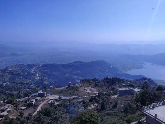 A panoramic view of the Atlas Mountains with paragliders dotting the sky and vibrant green valleys below.