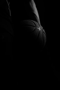 Close-up of a basketball player gripping a ball, veins and determination visible under stadium lights.