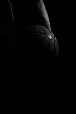 Close-up of a basketball player gripping a ball, veins and determination visible under stadium lights.