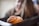 A close-up view of a freshly baked pastry with a flaky texture and a dusting of powdered sugar. The pastry is in the foreground, appearing warm and inviting. The background is blurred, possibly indicating a setting in a cafe or kitchen.