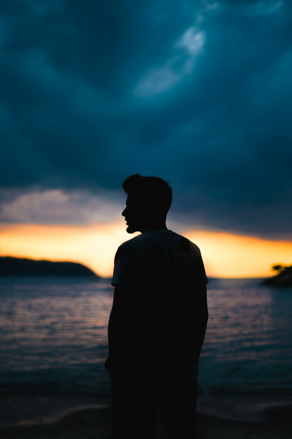 silhouette of man standing near body of water during sunset