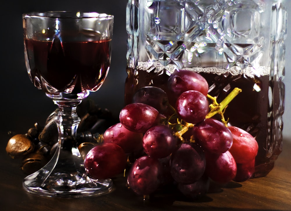 frutta rotonda rossa accanto al bicchiere da vino trasparente