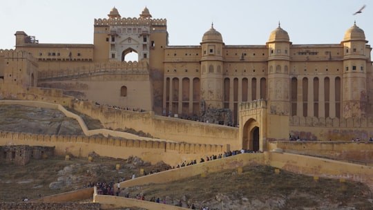 people walking on snow covered field near brown concrete building during daytime in Amer Palace and Fort India