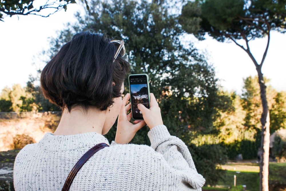 Frau in grauem Pullover fotografiert tagsüber grüne Bäume