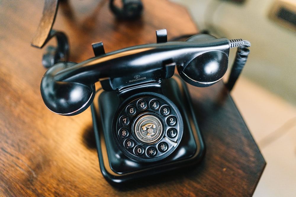 telefone rotativo preto na mesa de madeira marrom