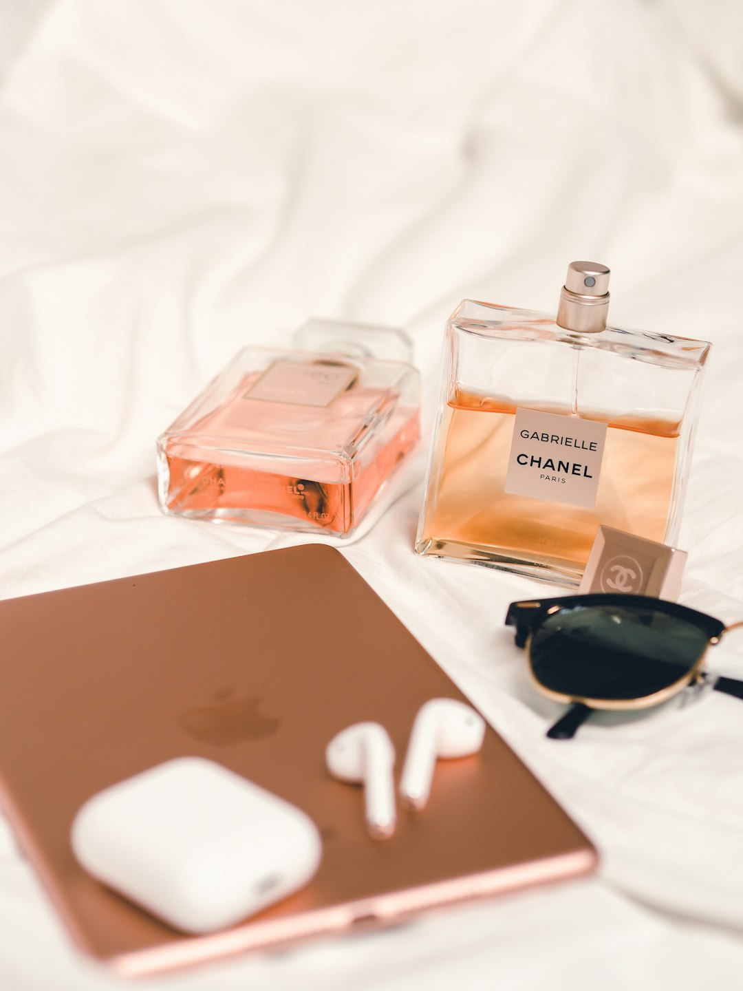 white and black sunglasses beside white earbuds and brown and white perfume bottle