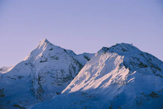 A serene close-up of icy mountain peaks glowing softly under a pastel sunset sky.
