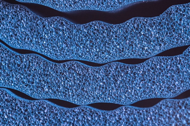 A close-up view of textured, wavy blue lines that resemble organic or cellular structures. The surface appears porous and detailed, with each line containing numerous small cavities or bubbles.