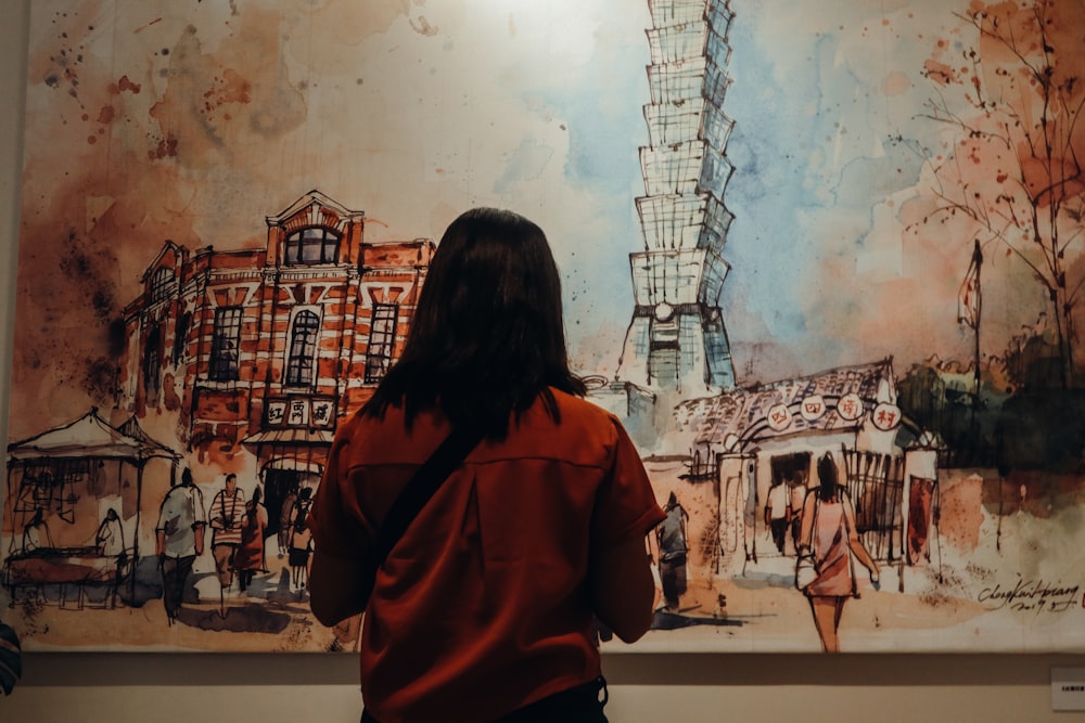 woman in orange jacket standing in front of building painting