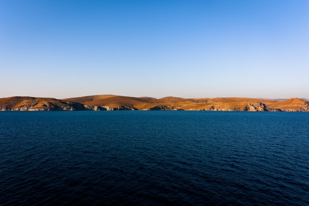 brown mountain beside body of water during daytime