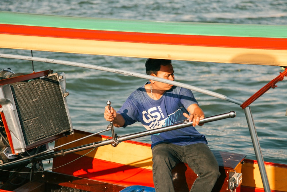 homem em camisa azul e jeans jeans azul sentado no barco vermelho e amarelo durante o dia